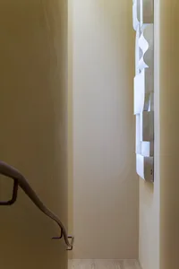 A vertical metal railing enhances the modern design of a stairwell, adorned with a unique wall showcasing white sheets of pap