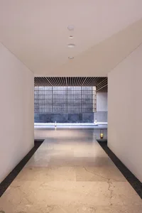 Long, spacious entrance hall with smooth marble tiles, leading to a black-framed glass wall.