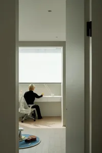 A modern home office desk setup with a person sitting at it, illuminated by a lamp.