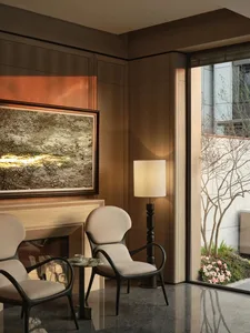 Modern living room with wood paneling, two beige upholstered chairs, and a floor lamp casting a warm light.