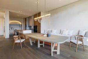 Modern living room and dining area featuring natural wood and concrete materials, with a long dining table, white sofa, and p