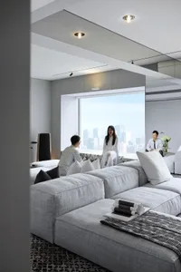 A modern living room featuring fabric couches, marble flooring, and a double-height window overlooking a cityscape.