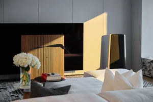 A modern living room with wooden accents, featuring a wooden cabinet, white cushions, and a vase of white flowers.