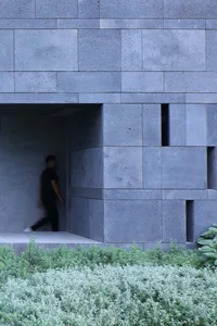 A modern minimalist concrete facade with a person walking in the background.