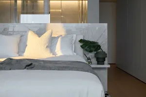 A minimalist bedroom featuring a marble headboard and a green plant on the nightstand.