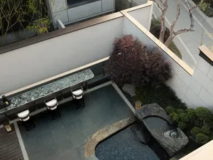 Modern outdoor terrace with stone and glass surfaces, featuring a seating area and water feature.