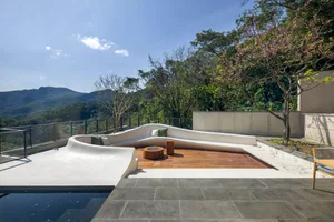A modern roof deck features a curvilinear concrete seating area with green cushions, a wooden fire pit table, and a view of t