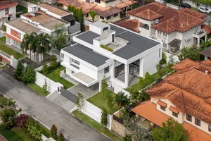 A modern white house with a white roof surrounded by other houses with brown tiled roofs and palm trees.