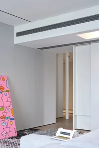 A modern living room featuring minimalist white paneling, with a pink artwork leaning against the wall and a stack of books o