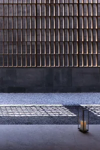 A close-up view of a metallic fence with concrete base casting shadows on the ground.