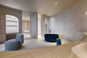 A minimalist bathroom with a round blue bathtub and concrete walls and floor.