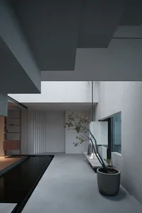 Minimalist living space with concrete walls, floor, and ceiling, featuring a potted plant and a bench.