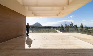 Man standing on a balcony with glass railings overlooking a landscape and mountains in the distance.