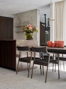 A modern dining room with wooden chairs and a marble table, featuring a vase of roses and red candles.