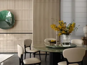 Modern dining room featuring a round glass-top table surrounded by white chairs, with a vase of yellow flowers and a green de