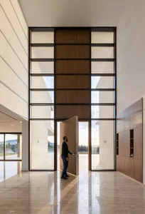 Man entering a modern building with a tall glass door and wooden accents.