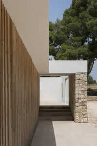 Exterior view of a modern farmhouse featuring a wooden fence, concrete columns, and stone steps leading up to a white wall.