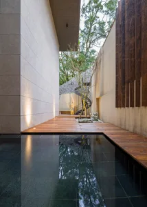 A modern interior space featuring a wooden pathway and a concrete pool reflecting the surrounding environment.