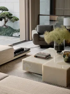 Modern living room with a marble table, beige sofa, and a bonsai tree outside the window.