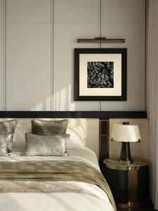A modern minimalist bedroom with grey fabric bedding, metallic grey pillows, and a matte black table lamp with a white shade.