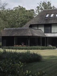 A modern residential home with a thatched roof and a grassy lawn surrounded by greenery.