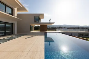 A modern residential pool deck featuring concrete surfaces and a large infinity pool.