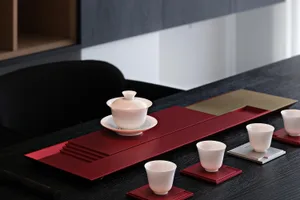 A beautifully arranged tea ceremony set featuring ceramic cups and bowls on a red tray.