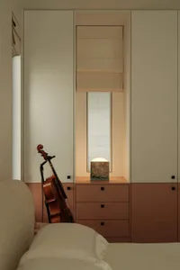 A minimalist bedroom with a white and brown cabinet, a basin, and a cello leaning against the wall.