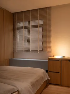 A minimalist bedroom featuring wooden blinds and a bed covered with a beige duvet.