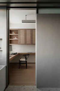A modern minimalist home office with wooden furniture and cabinets, featuring a sleek desk and a comfortable chair.