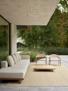 Modern minimalist outdoor living space featuring a sleek, low-profile sofa and wooden chairs, all set on a natural fiber rug 