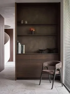 A modern bookshelf with a chair in front of it, featuring a minimalist design with dark wood materials.