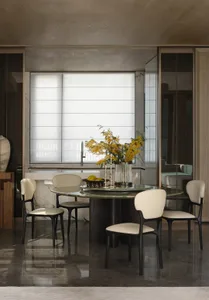 Modern dining room featuring a marble table and chairs, with a vase of yellow flowers and a bowl of fruit in the center of th