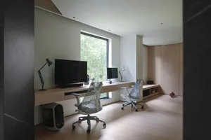 A modern home office featuring a wooden desk, ergonomic chairs, and a large window with a view of greenery.