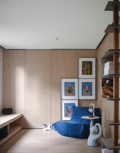A modern living room with wooden walls, a blue lounge chair, and framed portraits of dogs.