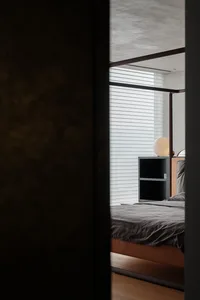 A modern minimalist bedroom with a bed, nightstand, and lamp.