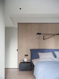 A modern minimalist bedroom featuring wooden paneling, a blue upholstered bed, and a sleek black floor lamp.