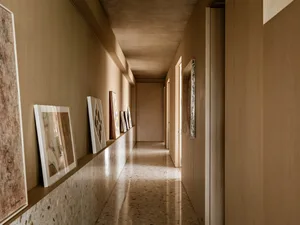 A minimalist corridor with a concrete wall and terrazzo floor, showcasing abstract art hanging along the walls.