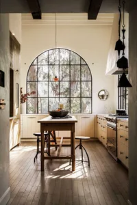 Industrial-style kitchen with large arched window, wooden floor, and high ceilings