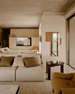 A minimalist living room featuring concrete walls and furniture with earthy tones and textures.