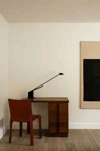 A minimalist office space featuring a wooden desk and a red leather chair under a modern floor lamp.