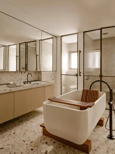 A modern bathroom featuring a white bathtub with a wooden bench, terrazzo flooring, and a glass-enclosed shower.