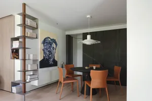Modern dining room featuring a round black table surrounded by four orange chairs, a bookshelf filled with books, and a large