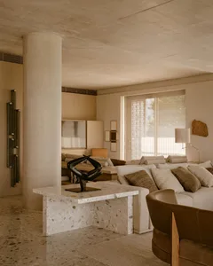 Modern living room with concrete walls, white couch, marble coffee table, and abstract sculpture.