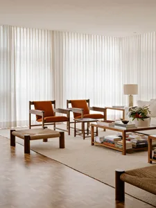 A spacious, modern living room with neutral-toned decor, including orange upholstered chairs, a wooden coffee table, and a la