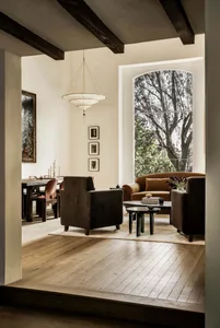 A modern living room with concrete walls and wooden flooring. Features include a large window, comfortable seating, and minim