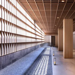 A modern interior design featuring a lobby with a concrete floor, wood accents, and a wooden ceiling with visible beams.