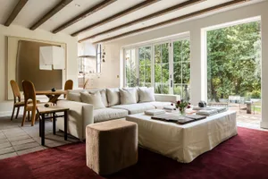 Modern living room with a white sectional sofa, wood floors, and large windows overlooking greenery.