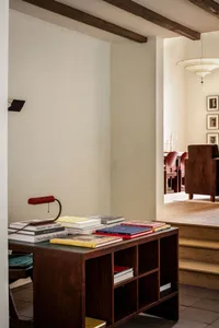 A cozy living room with warm wooden furniture, a bookshelf filled with books, and a lamp on a desk.