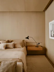 A minimalist bedroom featuring textured wall paneling, a bed with soft linens, and a sleek, floating nightstand with a modern